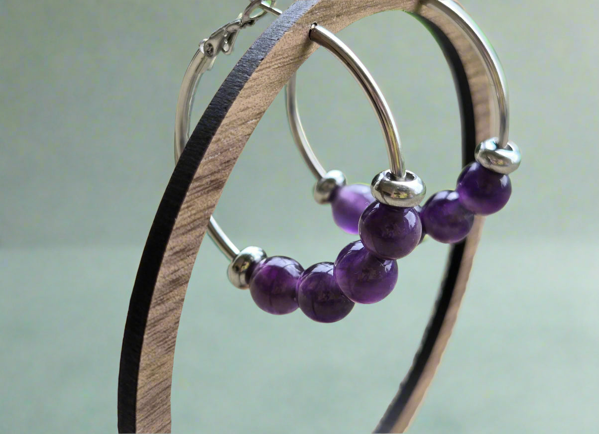Beaded hoop earrings with purple beads on a wooden stand outdoors.