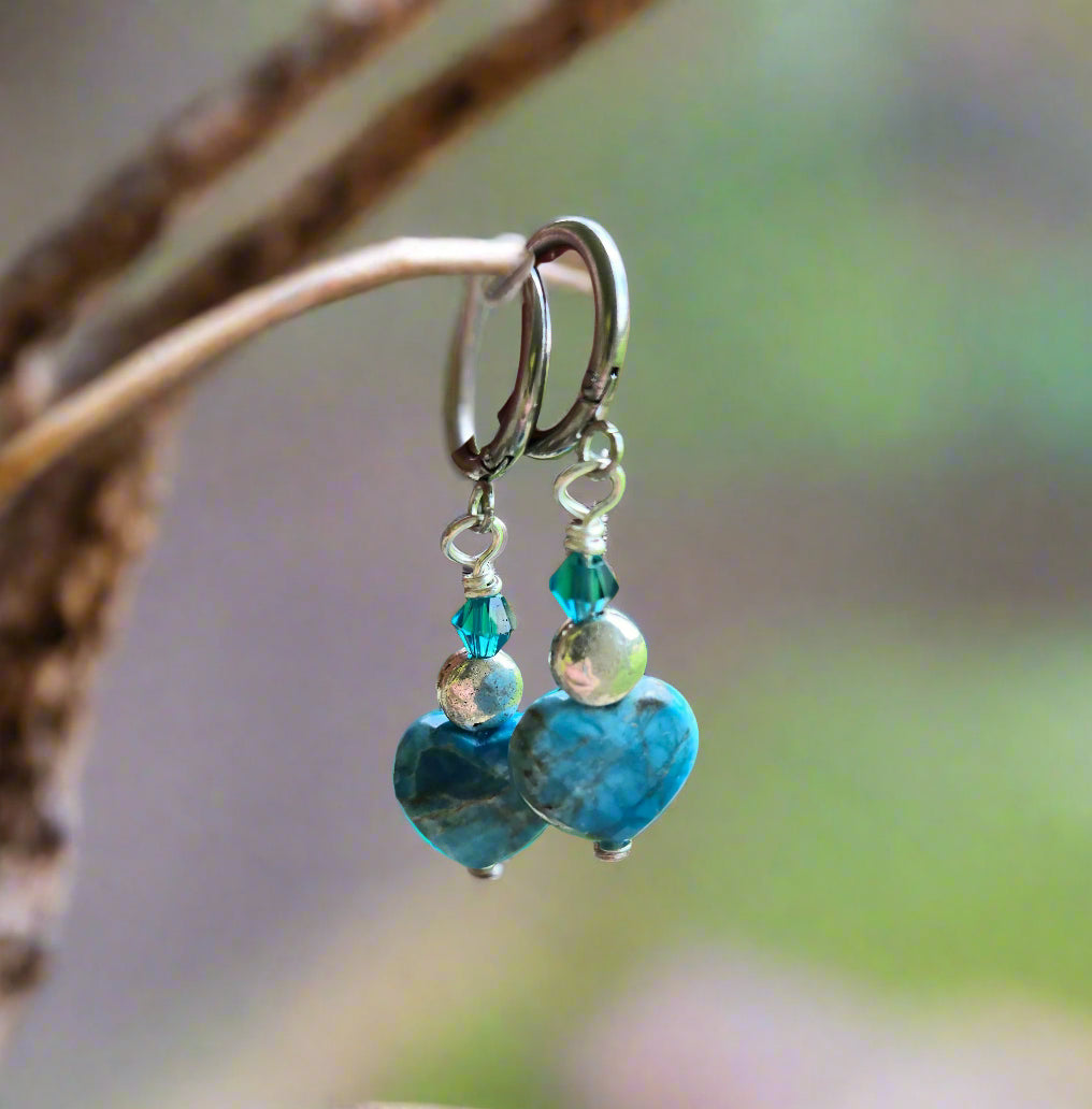 Hand holding a pair of blue beaded earrings with a blurred green outdoor background