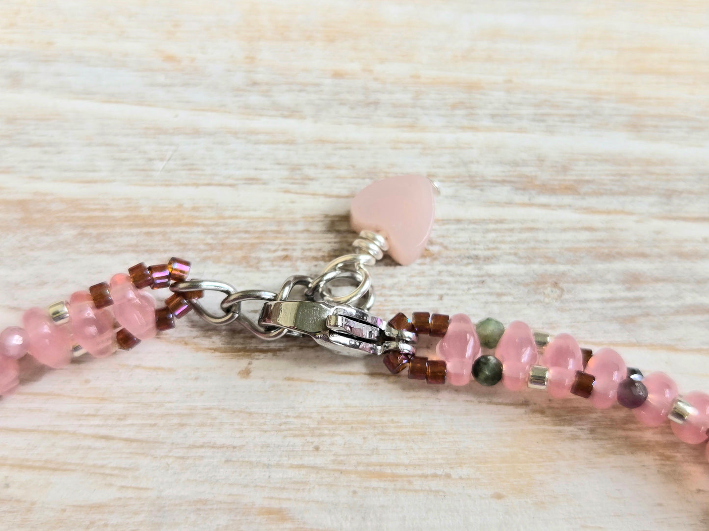 Beaded bracelet with pink and green stones on a light wooden surface