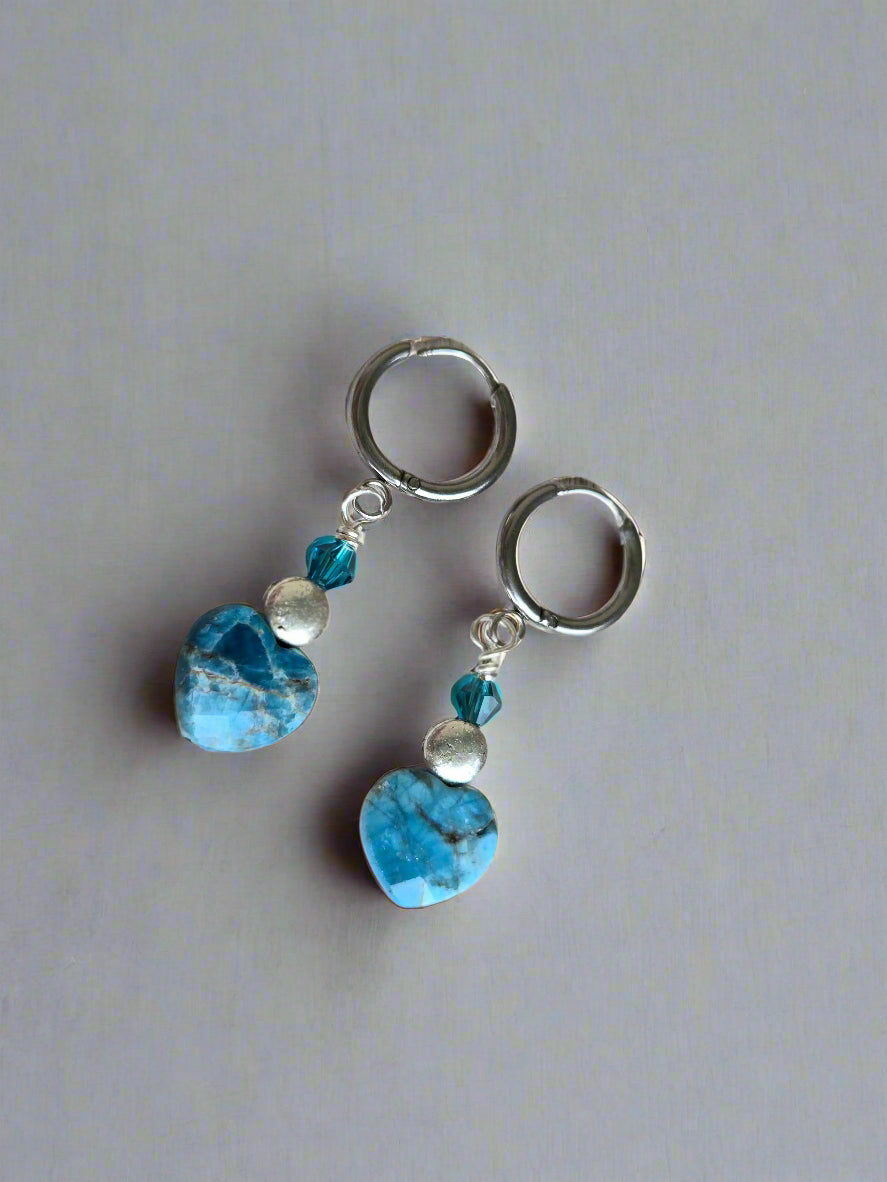 Pair of earrings with blue stones and silver accents on a light wooden surface