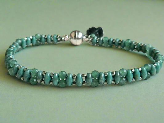 Green beaded bracelet with silver clasp on a light wooden surface