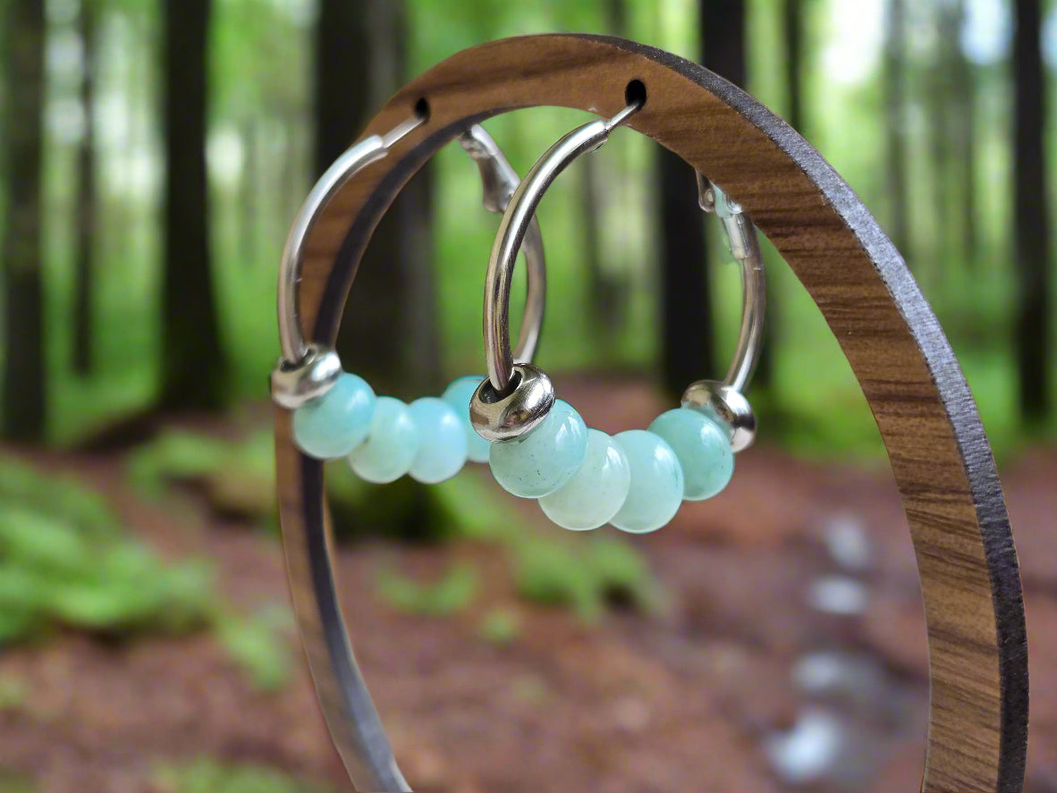 Hoop earrings with amazonite beads on a wooden stand against a blurred background