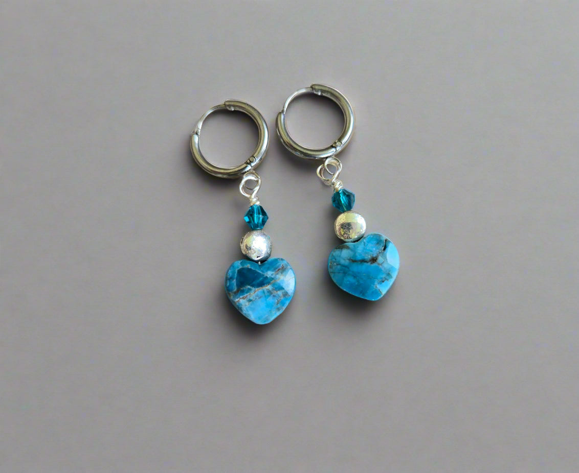 Pair of hoop earrings with blue heart-shaped apatite stones on a wooden surface