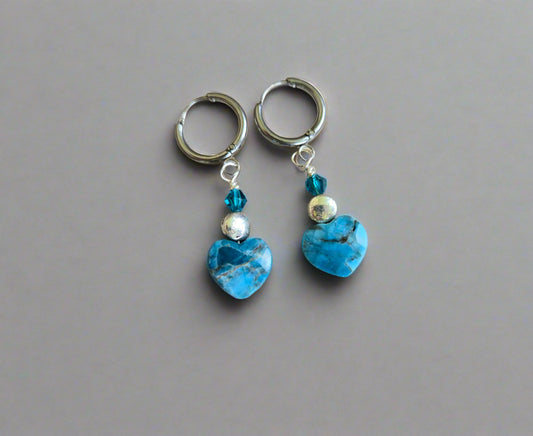 Pair of hoop earrings with blue heart-shaped apatite stones on a wooden surface