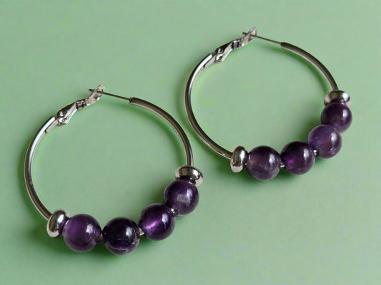 Hoop earrings with purple amethyst beads on a wooden surface