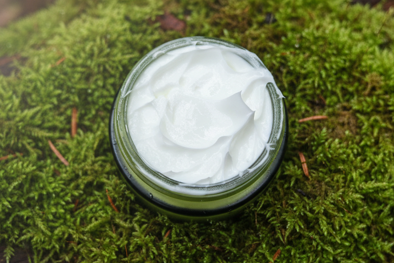Jar of white cream on a green moss background